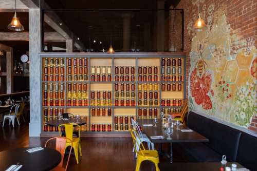 Interior of a restaurant featuring a wall of jars and colorful chairs, with a mural of bees and honeycomb.