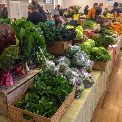 A vibrant farmers market display featuring various fresh greens and vegetables in baskets and crates.