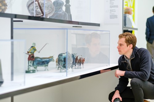 A man examines glass animal sculptures displayed in a gallery case.