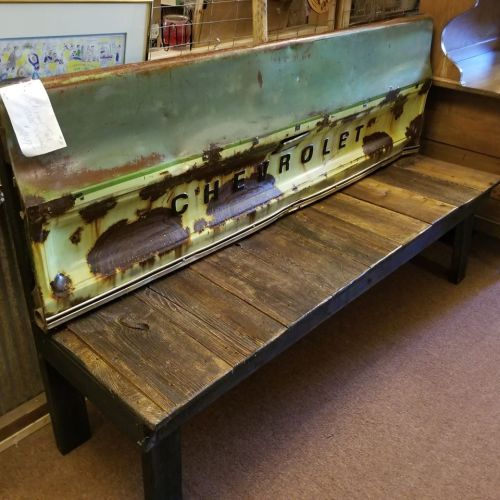 A rustic bench made from a vintage Chevrolet truck bed, featuring a weathered wood base and a green and yellow backrest.