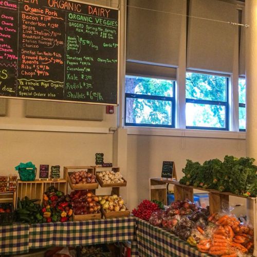A market display featuring organic veggies and dairy, with various produce and price signs on a checkered tablecloth.