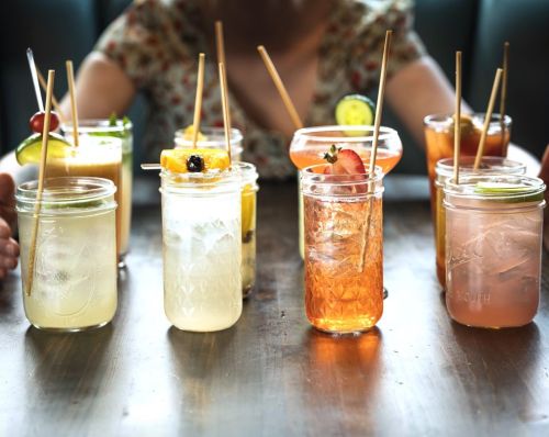 A variety of colorful cocktails in mason jars, garnished with fruit and served on a wooden table.