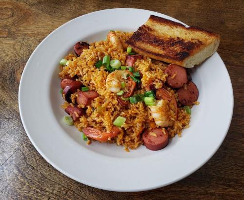 A plate of shrimp and sausage fried rice garnished with green onions, accompanied by a slice of toasted bread.