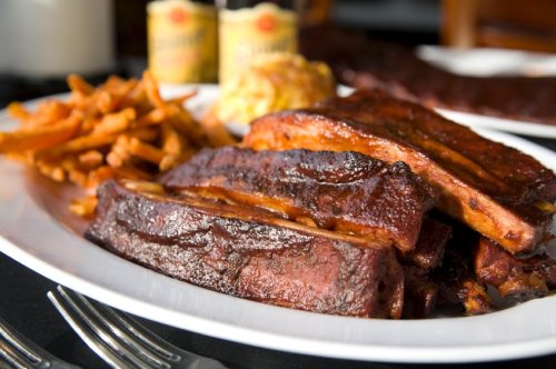 A plate of succulent barbecue ribs with crispy sweet potato fries and a cornbread muffin, served with two sauces.