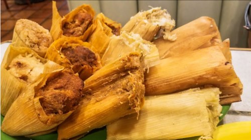 A colorful assortment of tamales wrapped in corn husks, displayed on a green plate.