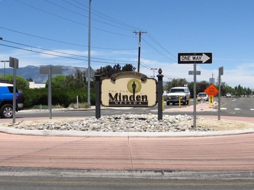 Welcome sign for Minden, Nevada, with a roundabout and directional signs in a sunny landscape.