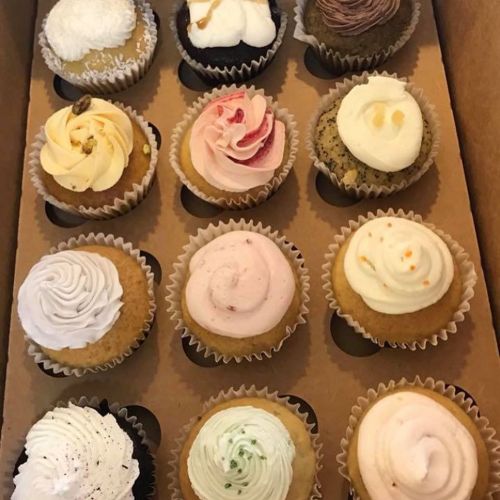 A box of twelve assorted cupcakes with various frosting designs and colors.