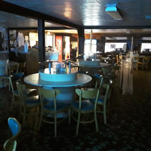 Dimly lit interior of a restaurant with empty tables and chairs, featuring a Coca-Cola vending machine in the background.