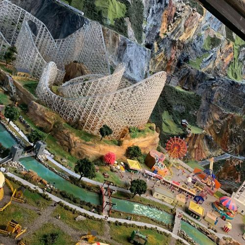 A detailed miniature amusement park featuring a roller coaster, ferris wheel, and scenic landscapes.