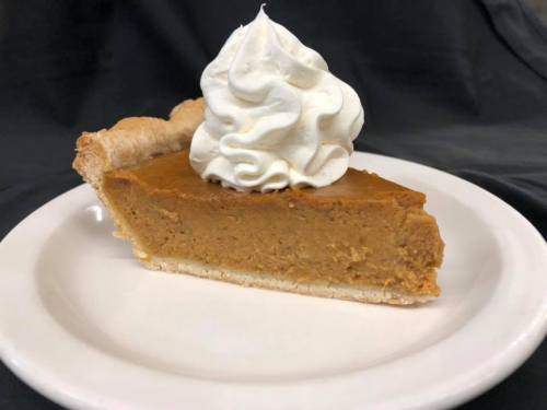 A slice of pumpkin pie topped with whipped cream on a white plate, set against a dark background.
