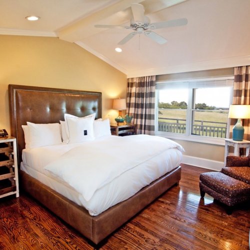 Cozy bedroom with a large bed, wooden floors, and a window overlooking a scenic view. Stylish decor and soft lighting.