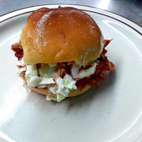 A soft bun filled with shredded chicken and creamy coleslaw, served on a white plate.