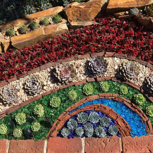 Colorful garden mosaic featuring succulents, stones, and glass in a wave pattern with red, green, and blue hues.