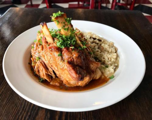 A plate of tender braised meat with bone, served over creamy risotto and garnished with fresh herbs.