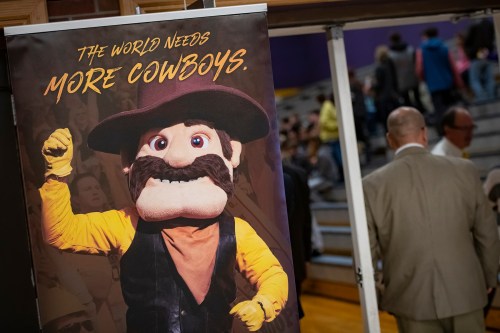 A large puppet of a cowboy with a mustache stands next to a banner reading "The world needs more cowboys."