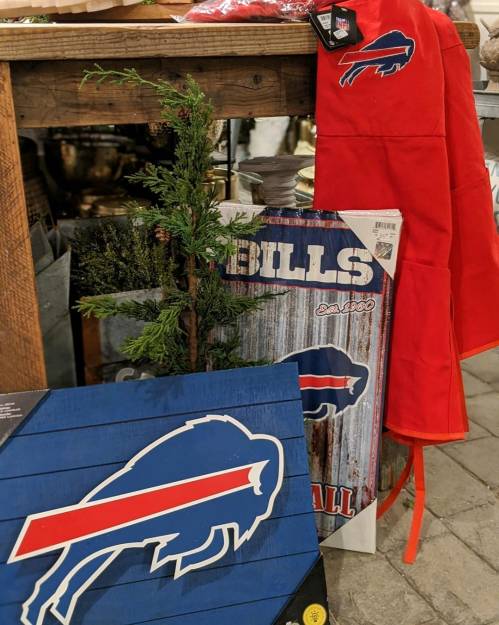 Buffalo Bills merchandise displayed, including a red apron, a sign, and a blue wooden plaque, with greenery in the background.