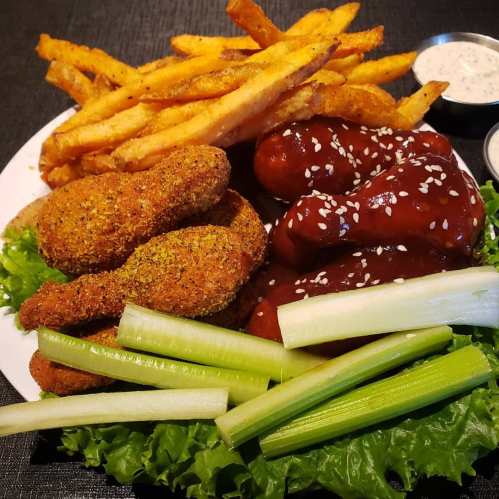 A plate of crispy fried chicken, BBQ wings, celery sticks, and golden French fries on a bed of lettuce.