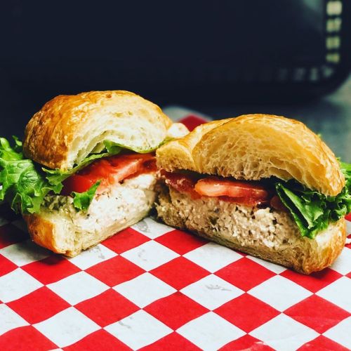 A croissant sandwich filled with chicken salad, lettuce, and tomato, resting on a red and white checkered paper.