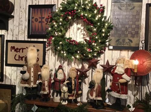 A festive display featuring Santa figurines, a wreath, and holiday decorations on a rustic wooden wall.