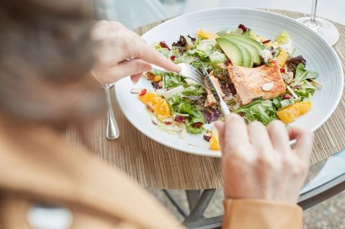 A person is enjoying a fresh salad with salmon, avocado, and citrus on a wooden table.