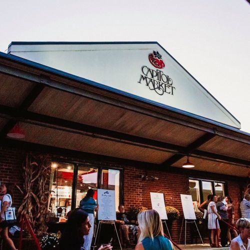 Exterior of Capitol Market with people gathered outside, featuring a sign and decorative autumn elements.