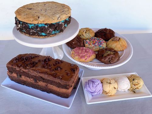 A display of desserts featuring a large cookie sandwich, assorted cookies, and a slice of chocolate cake with ice cream.