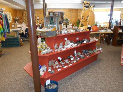 Display of various rocks and minerals on red shelves in a shop, with labels and decorative items in the background.