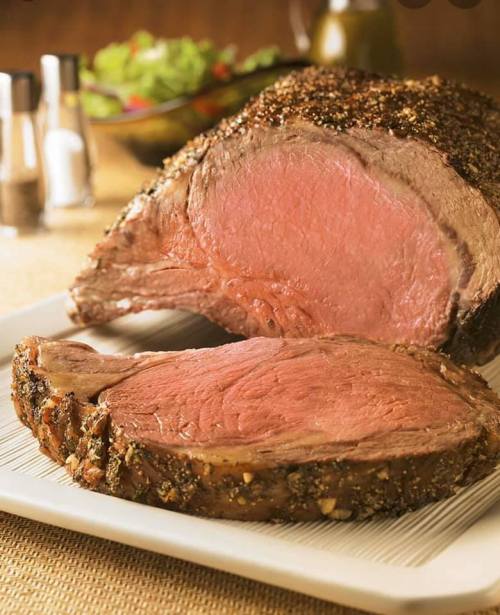 A perfectly cooked roast beef with a juicy pink center, served on a white platter with a side salad in the background.