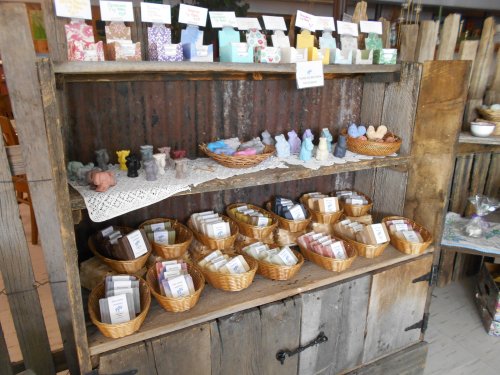 A rustic display shelf with baskets of handmade soaps and decorative figurines on a wooden background.