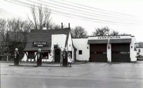 Historic gas station with a unique building design, featuring vintage pumps and a service garage. Black and white photo.
