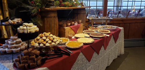 A festive dessert table featuring various cakes, pies, and pastries, decorated with holiday greenery.