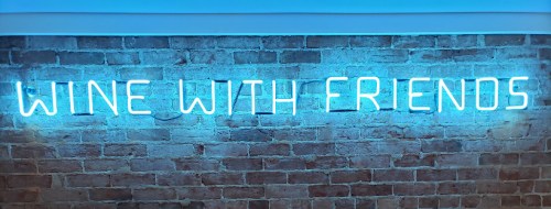 Neon sign on a brick wall that reads "WINE WITH FRIENDS" in bright blue letters.