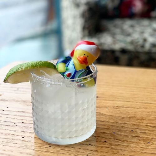 A margarita glass with a salted rim, featuring a small rubber duck wearing a Santa hat and a lime wedge.