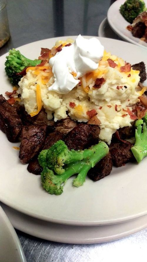 A plate of steak topped with mashed potatoes, cheese, bacon, and sour cream, accompanied by broccoli.
