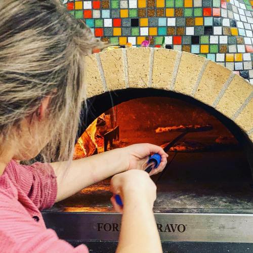 A person using a tool to manage a fire inside a colorful, tiled pizza oven.