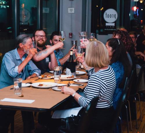 A group of people at a dinner table raising glasses in a toast, enjoying food and drinks together.