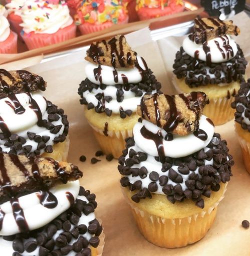Delicious cupcakes topped with chocolate drizzle, mini chocolate chips, and cookie pieces on a creamy frosting base.