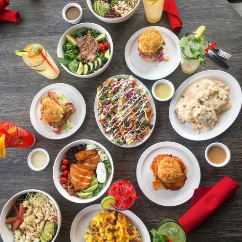 A vibrant spread of various dishes, including salads, burgers, nachos, and drinks, arranged on a wooden table.