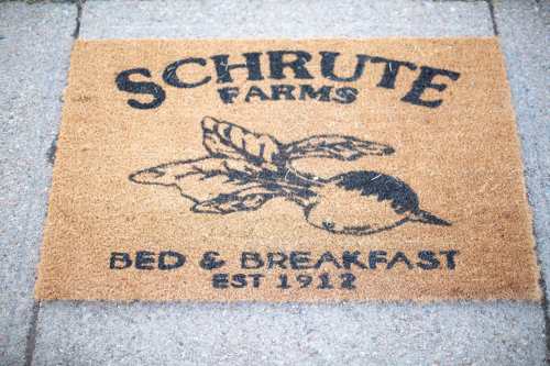 A doormat featuring "Schrute Farms Bed & Breakfast" with a beet illustration, established in 1912.
