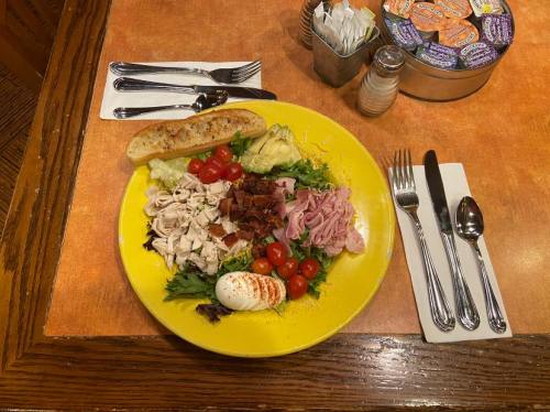 A colorful salad with turkey, ham, bacon, cherry tomatoes, and a boiled egg, served with a toasted breadstick.