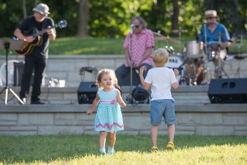 Two children play in a grassy area while a band performs on stage in the background.