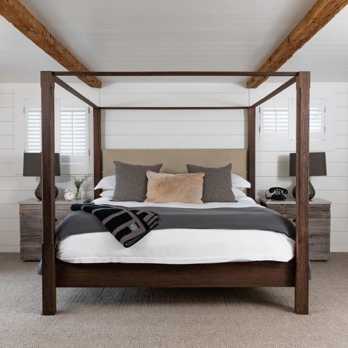 A cozy bedroom featuring a four-poster bed, neutral bedding, and wooden nightstands with lamps.