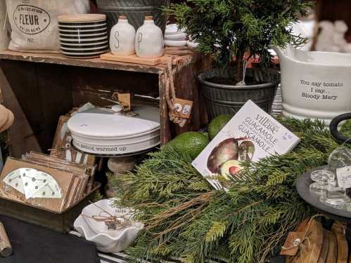 A rustic display featuring kitchenware, avocados, greenery, and a recipe for guacamole on a wooden table.