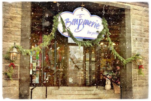 A festive storefront decorated with greenery and a snowman, surrounded by falling snowflakes.