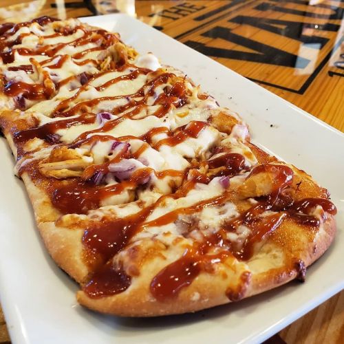 A flatbread pizza topped with barbecue sauce, chicken, cheese, and red onions, served on a white plate.