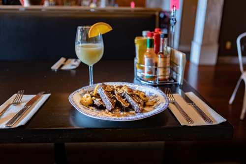 A plate of sliced beef with mushrooms, accompanied by a cocktail and a variety of hot sauces on a table.