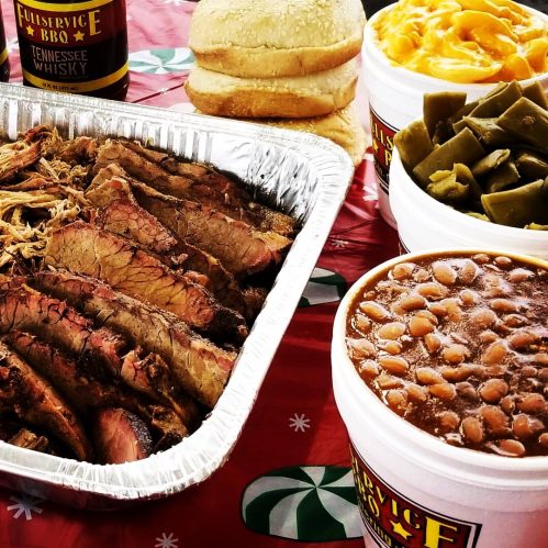 A platter of sliced brisket with sides of macaroni and cheese, green beans, and baked beans, alongside bread rolls.