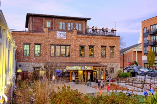 A brick building with a rooftop patio, featuring signs for Jekyll Brewing and Central City Tavern, surrounded by greenery.