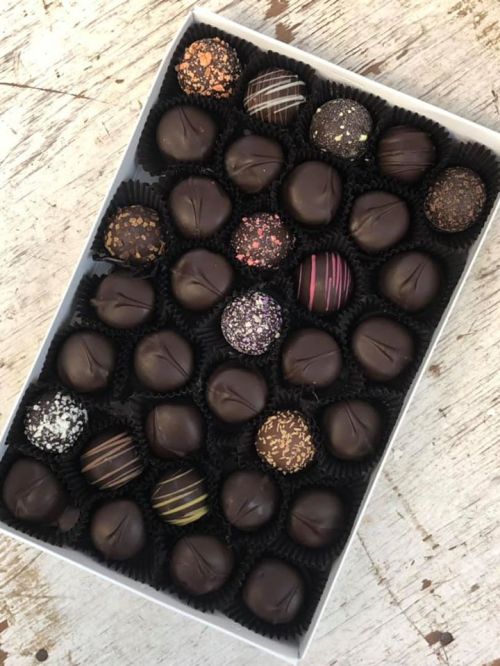 A box of assorted chocolate truffles, featuring various toppings and designs, arranged neatly in black liners.