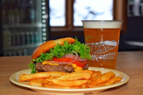 A juicy burger with lettuce, tomato, and cheese, served with fries and a pint of beer on a wooden table.